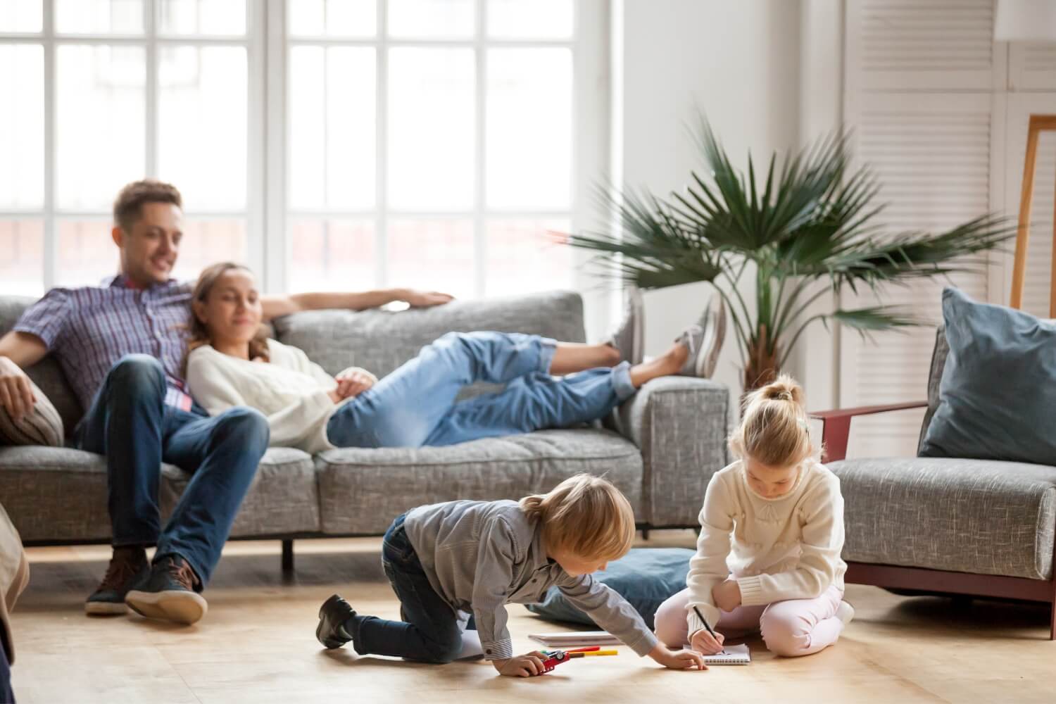 Children sister brother playing drawing together floor while young parents relaxing home sofa little boy girl having fun friendship siblings family leisure time living room